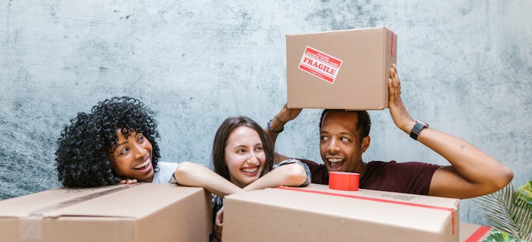 three people smiling while hiding behind cardboard boxes